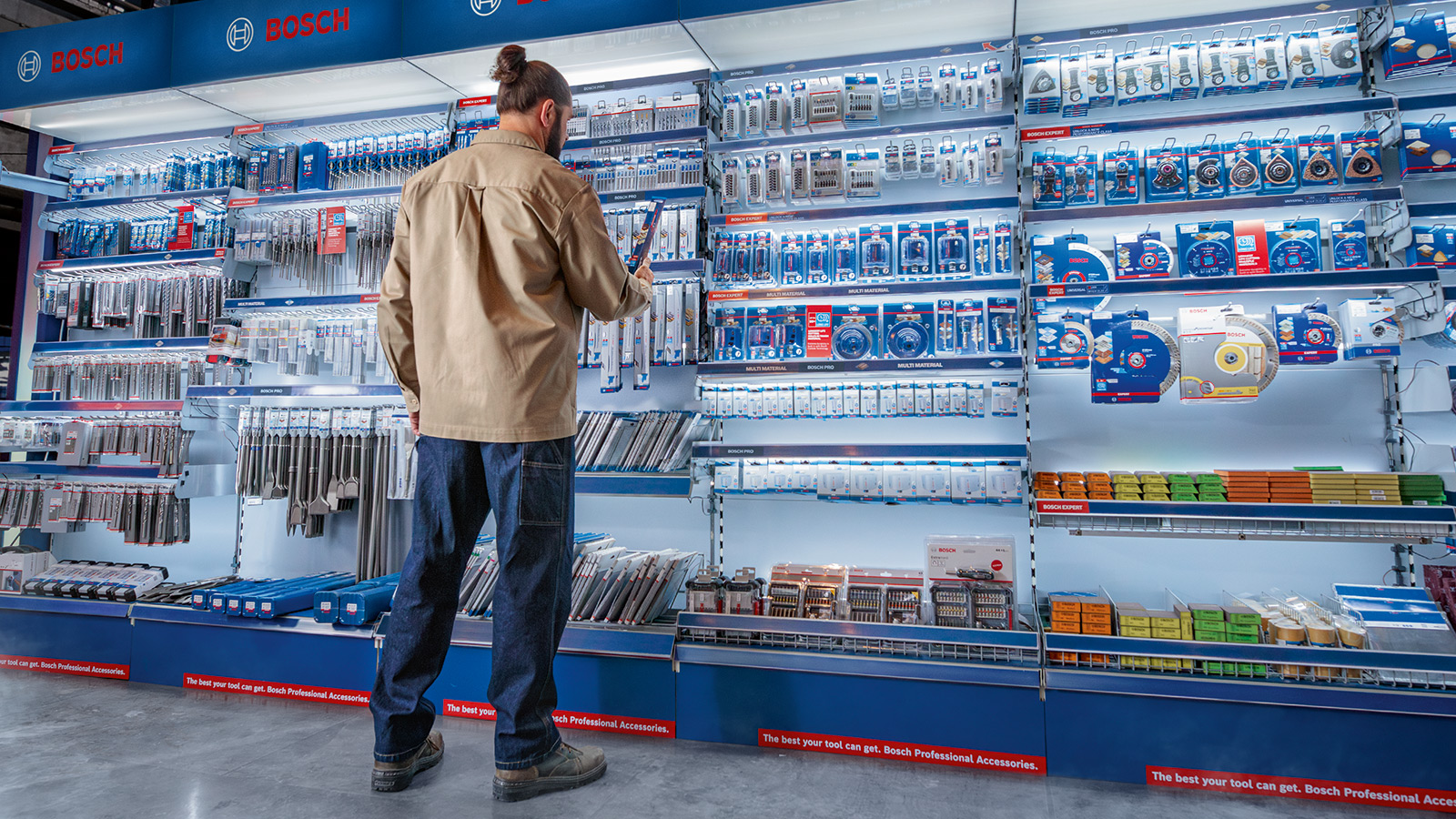 A man with sideburns stands in front of a shelf full of Bosch tools, including drills and accessories.