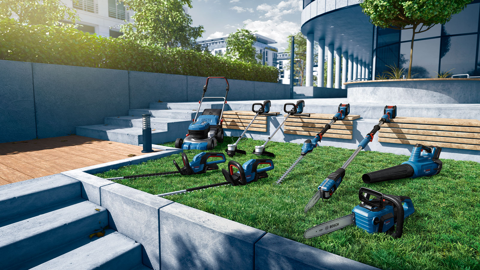 A selection of blue Bosch Professional garden tools is placed on green grass, surrounded by concrete steps and benches.