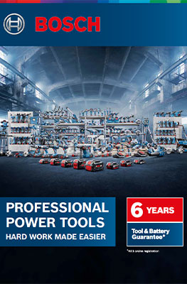 A variety of blue Bosch Professional tools is arranged in a large, bright warehouse. The tools are placed on shelves and tables, surrounded by boxes and accessories, creating a professional workshop atmosphere. In the background, tall windows are visible, letting in daylight.
