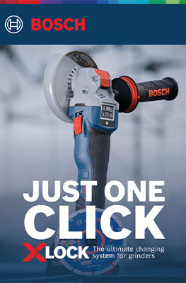 A blue Bosch Professional angle grinder with X-LOCK system stands on a bright workbench. Blurred in the background.