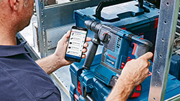 A man holds a Bosch Professional drill and a smartphone.