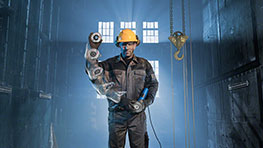 A worker in black protective clothing with a yellow helmet stands in a hall.
