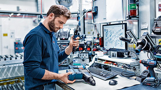 A worker checks a blue Bosch Professional cordless screwdriver at a table.