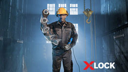 A worker in protective clothing with X-LOCK tool in a dark hall.