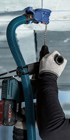 A person wearing gloves is using a Bosch cordless drill with a hose.