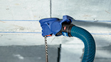 A blue Bosch Professional dust extractor on a wall with a drill.