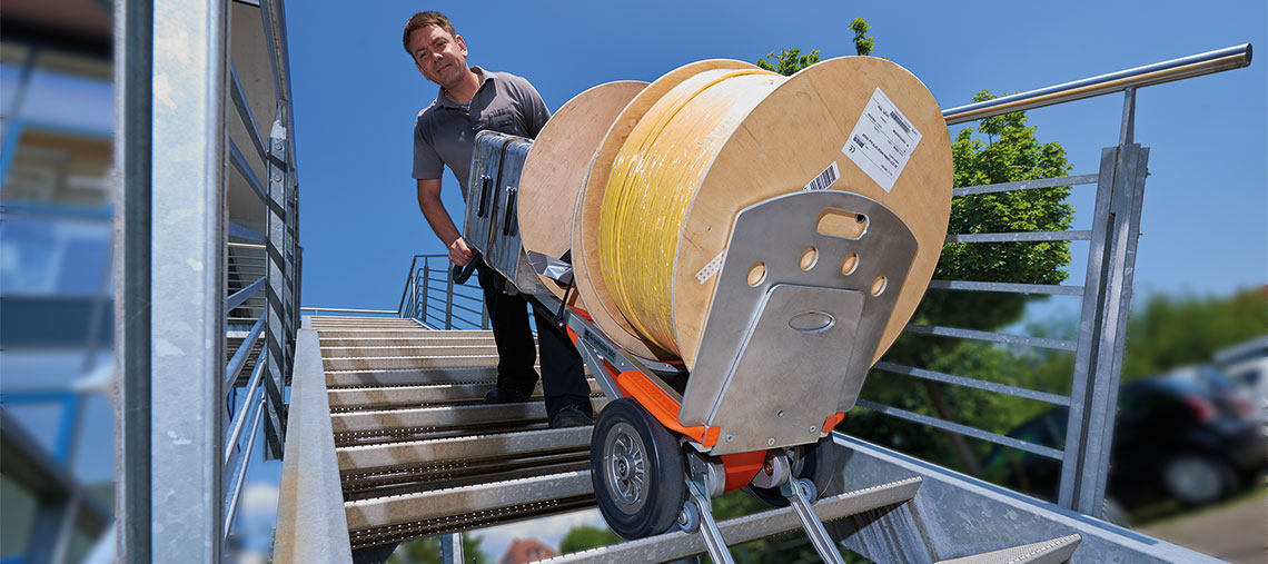 A man is pulling a roll of cable up the stairs with a hand cart.