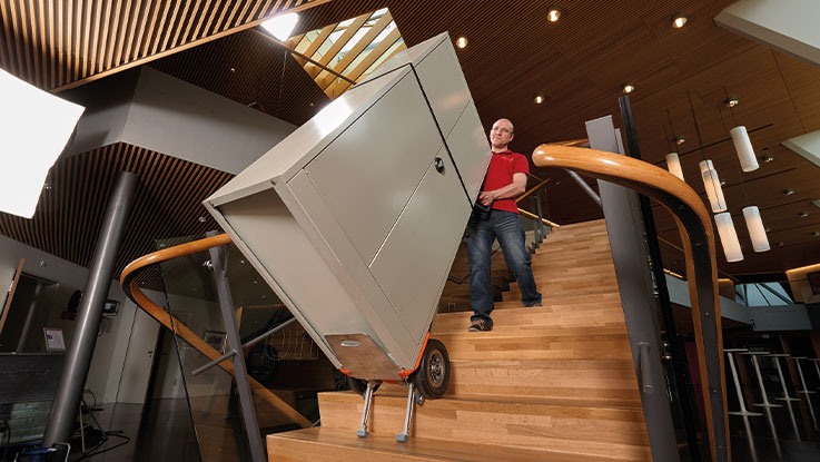 A man is carrying a large wardrobe up the stairs.