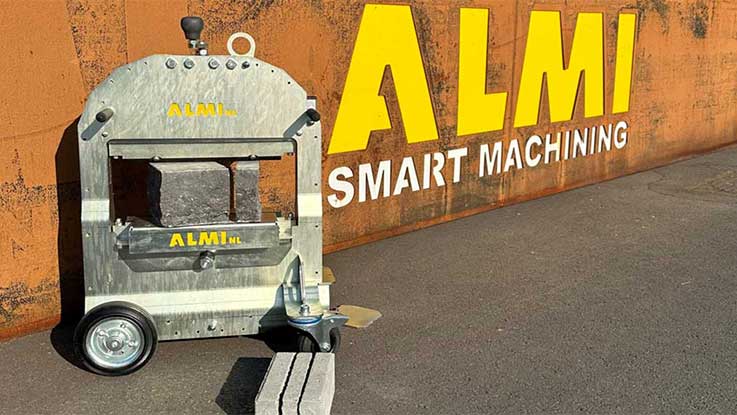 An ALMI machine stands in front of a rusty wall with yellow writing.