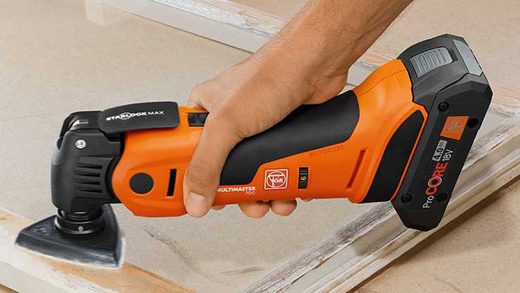 A hand holds an orange Bosch battery multitool on wood.