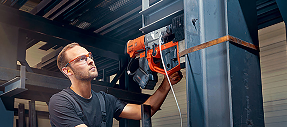 A man is using an orange Bosch nailer on a steel beam.
