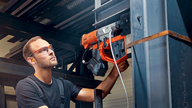 A man is using an orange Bosch tool on a metal beam.