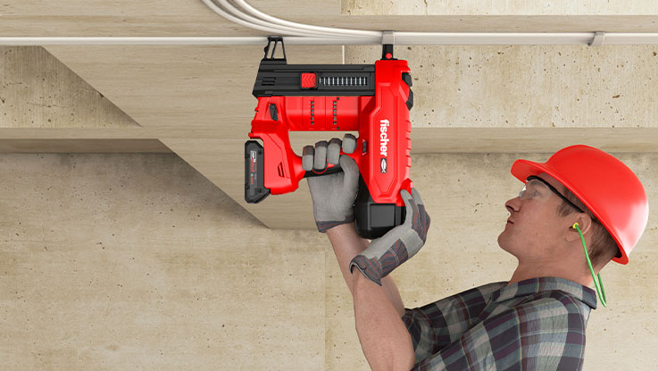 A man with a red helmet is using a red battery-powered nail gun.