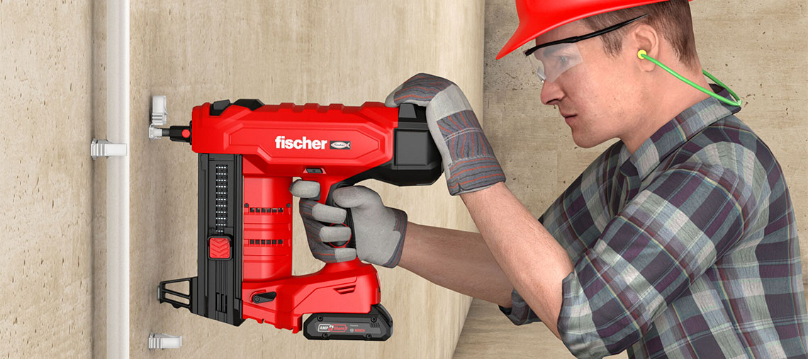 A man with a red helmet is using a red cordless nailer on a wall.