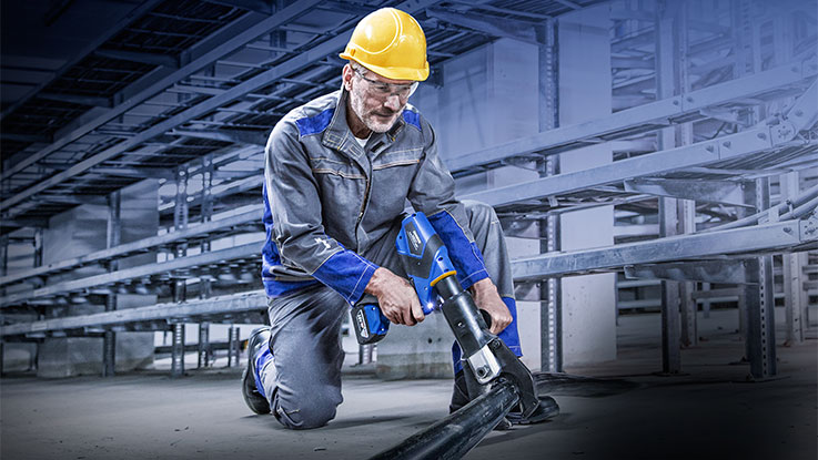 A man in work clothes is using a blue Bosch tool.
