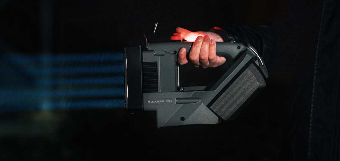 A hand holds a gray, illuminated tool with blue rays.
