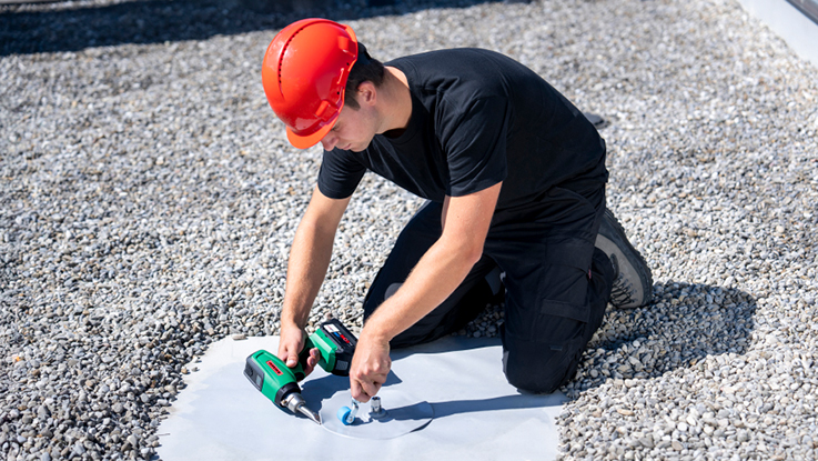 A craftsman in a red helmet is using a Bosch tool on the roof.