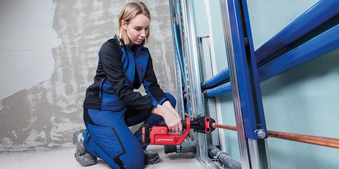 A woman in blue work clothes is using a red Bosch tool.