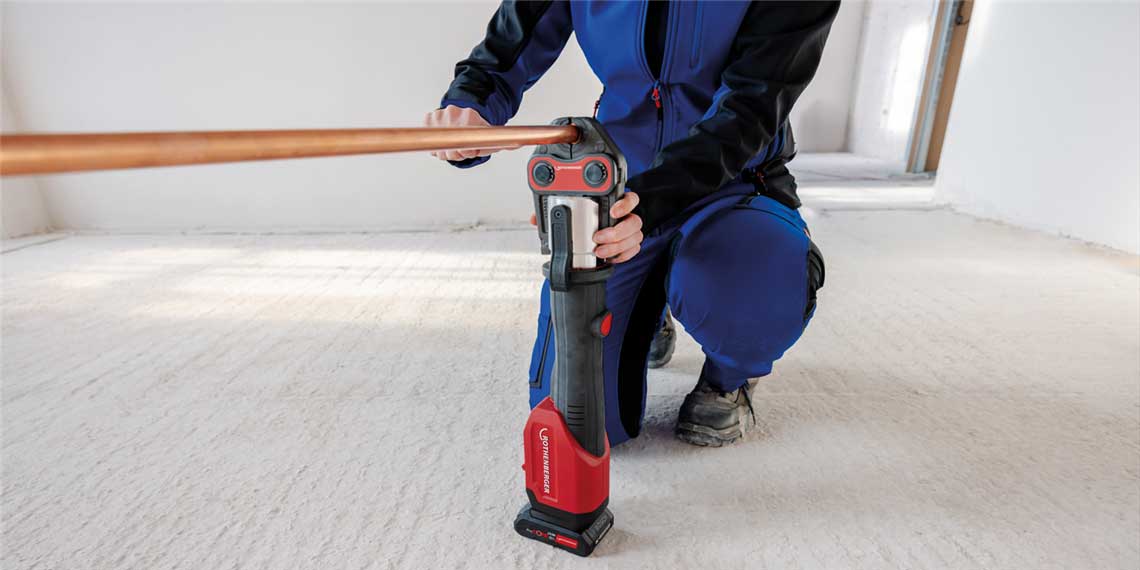 A craftsman is kneeling and using a red Bosch Professional pipe bender.