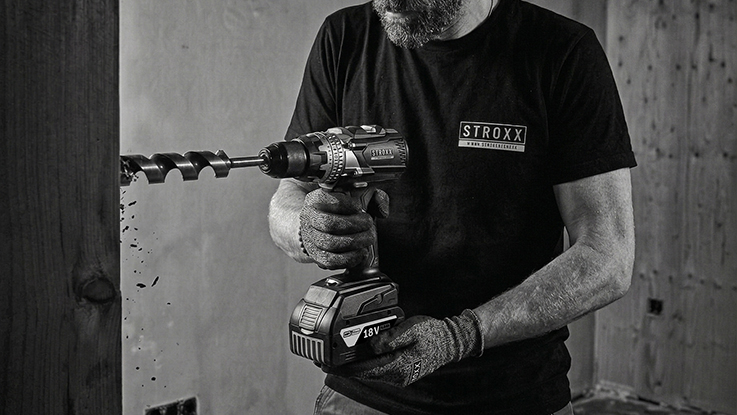 One hand holds a set of metal drill bits while a drill is ready in the other hand.