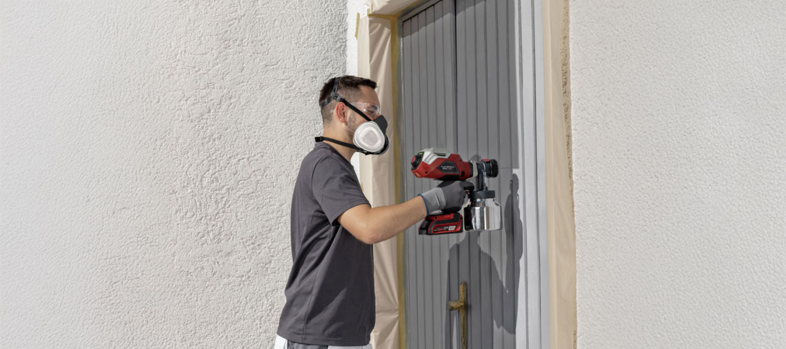 A man sprays paint on a gray door with a red Bosch tool.