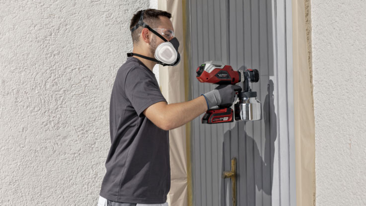 A man with a mask sprays color with a red Bosch tool on a door.