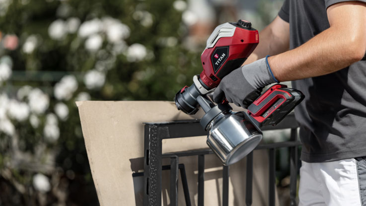 A red Bosch Professional paint sprayer is held against a wall.