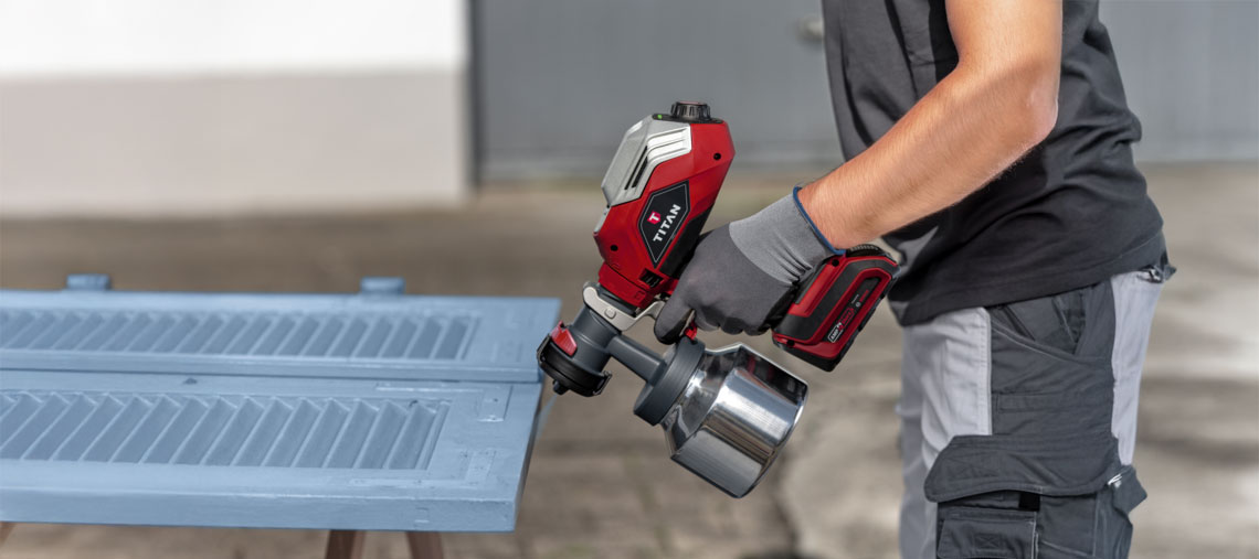 A red Titan spray paint device is being used by a person.