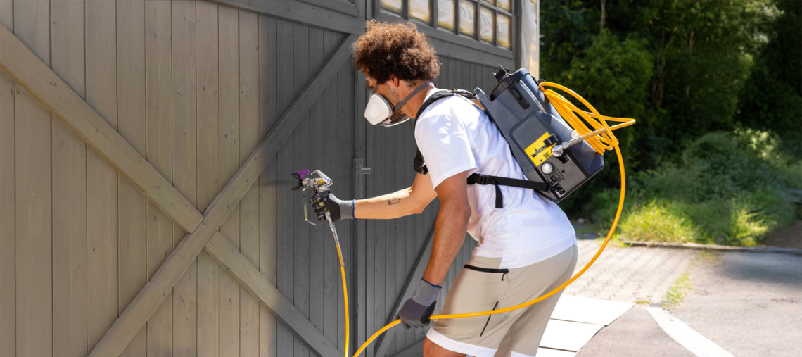 A man is spraying a wall outdoors with a Bosch paint device.