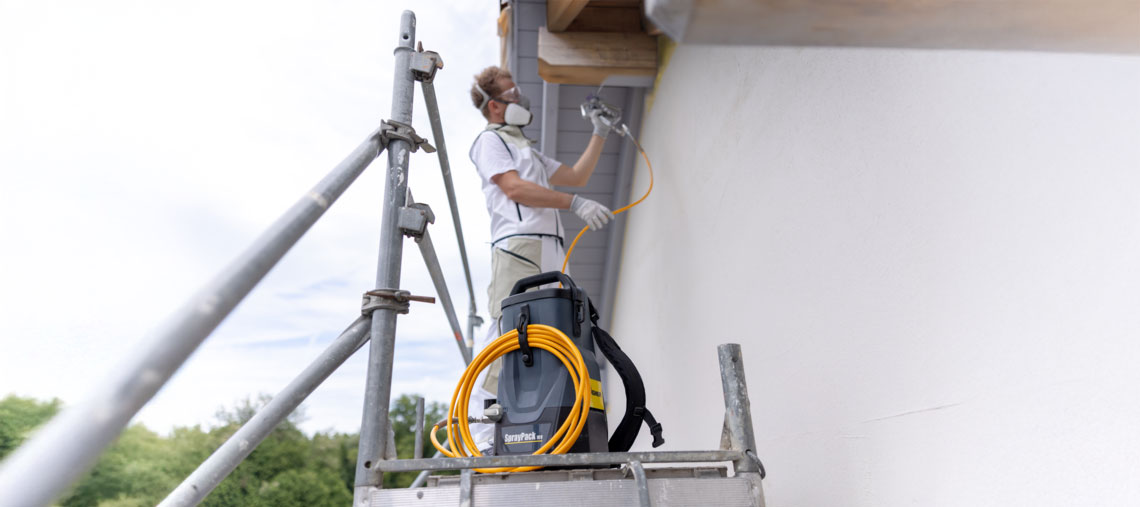 A craftsman on a scaffold is spraying paint with a spray machine.