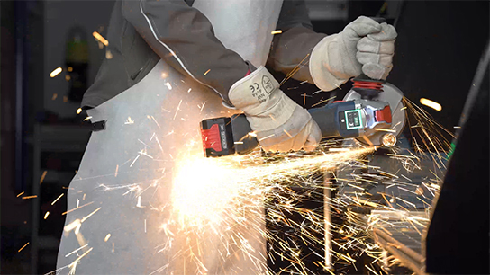 A worker wearing gloves uses a Bosch grinder, sparks fly.