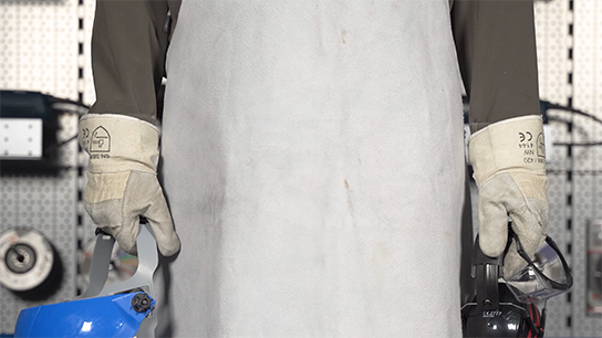 A worker wearing gloves holds a blue protective mask and a drill.