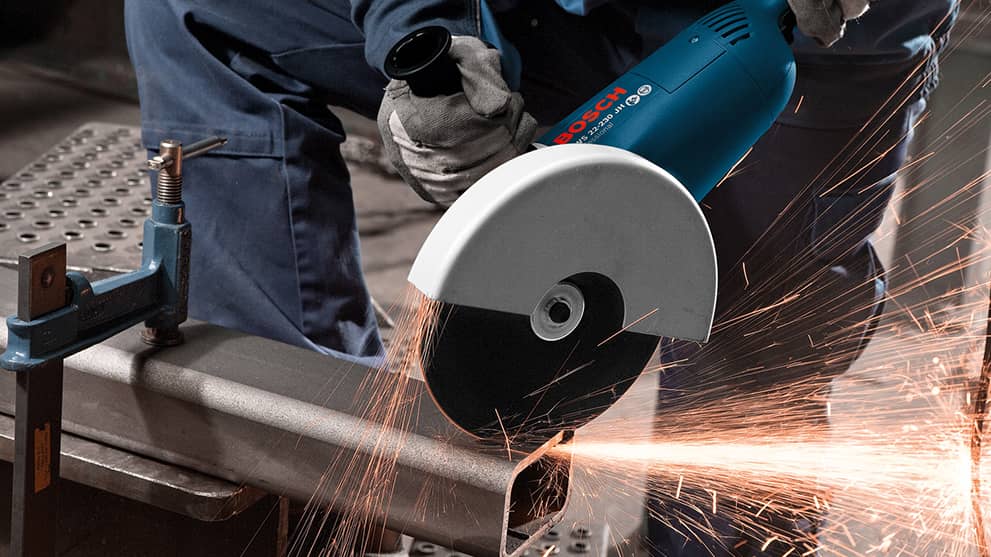 A Bosch Professional angle grinder cuts a metal pipe, sparks fly.