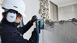 A worker wearing a helmet and hearing protection is working on a wall with a Bosch tool.
