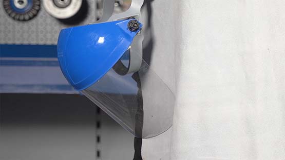 A blue safety helmet with a transparent visor cover is hanging on the wall.