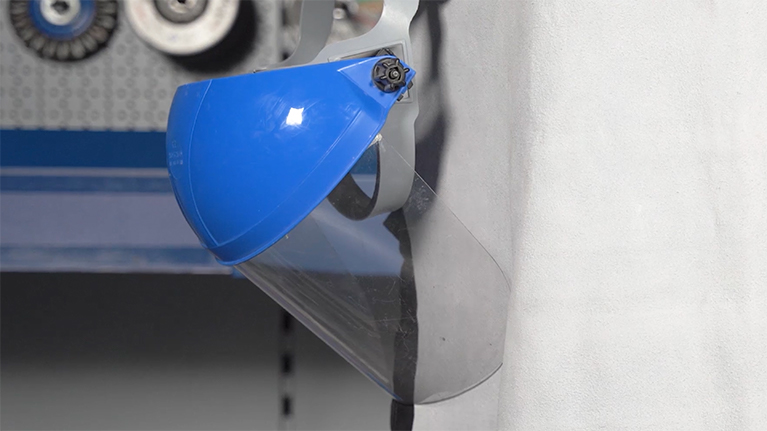 A blue safety goggles hangs on a wall, below are tools.