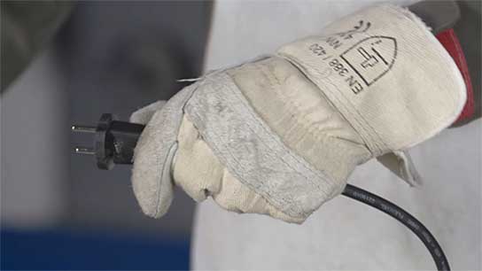 A hand in a gray work glove holds a plug.