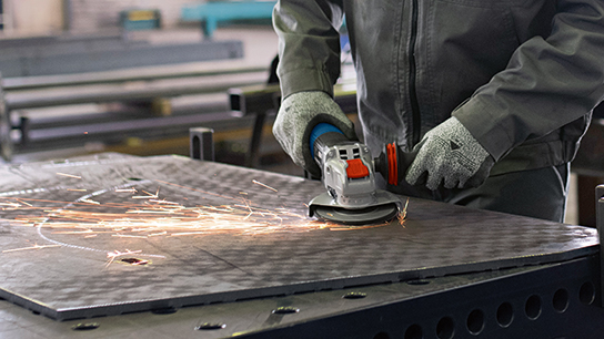 A worker is using an angle grinder on a metal table.