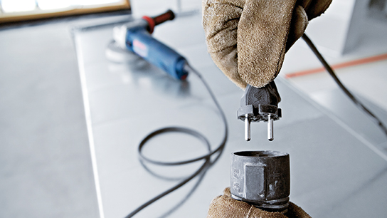 A gloved hand holds a plug above a tool.