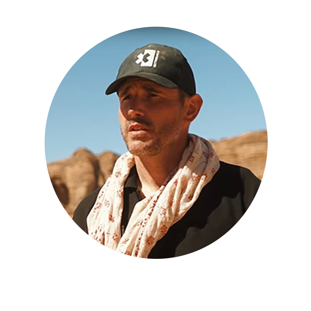 Kester Wilkinson, Event Manager of Extreme E Man with a black hat and beige scarf in a rocky desert landscape.