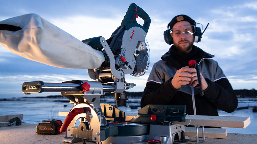 A Bosch Professional miter saw stands on a table, a man is working on it.