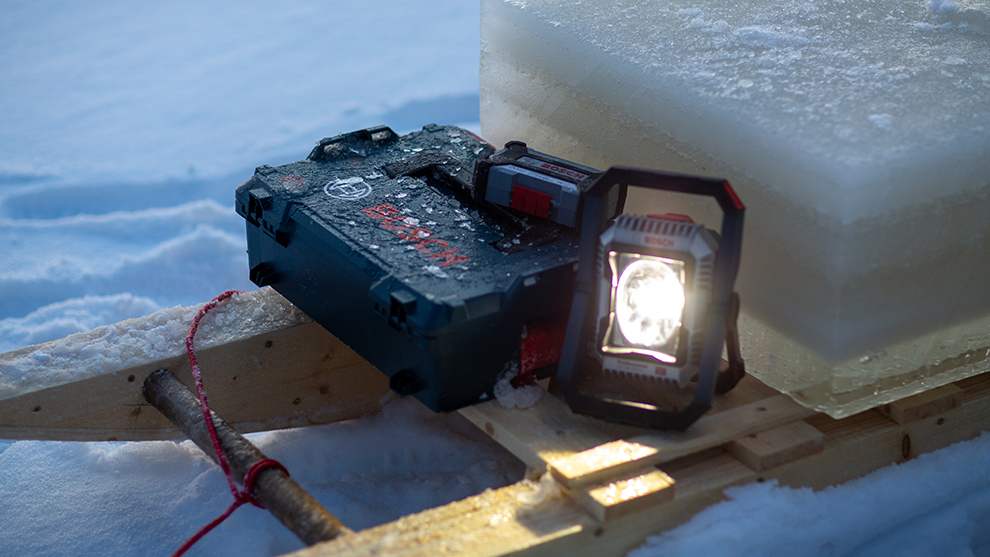 Bosch Professional battery lamp shines next to a toolbox in the snow.