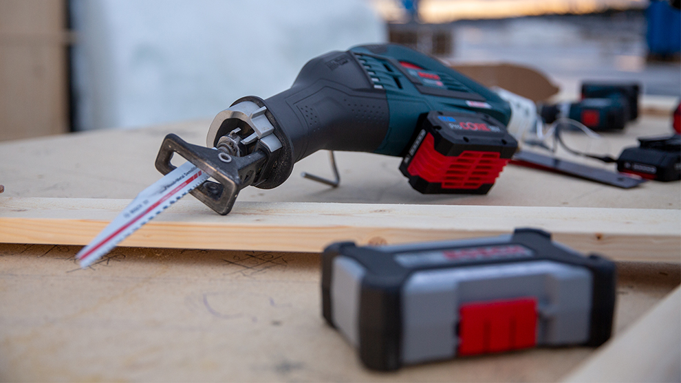 A black Bosch Professional saw with a red battery on a wooden board.