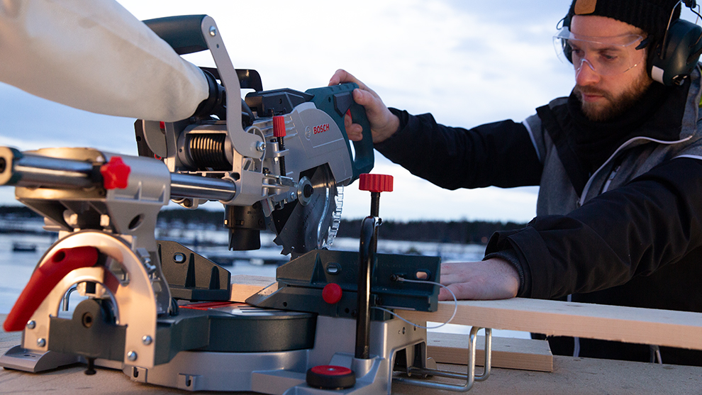 A man is using a Bosch Professional miter saw outdoors.
