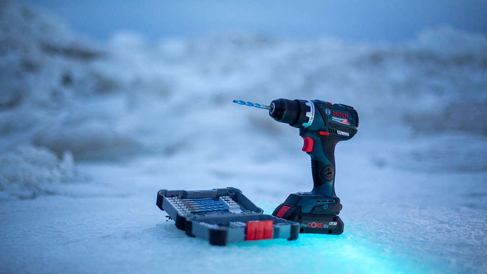 A Bosch Professional cordless drill stands on ice next to a bit set.