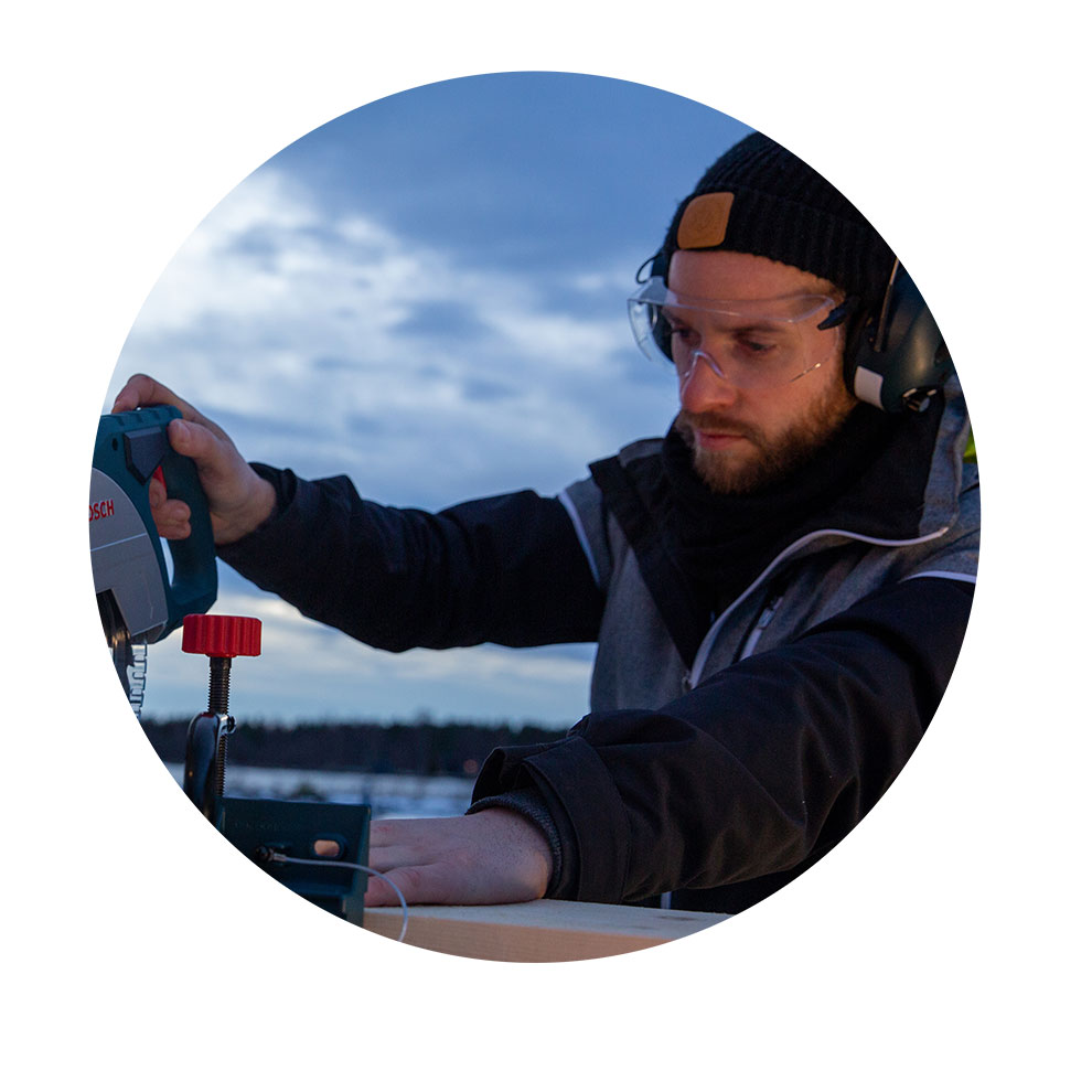 A man wearing safety glasses is using a Bosch jigsaw outdoors.