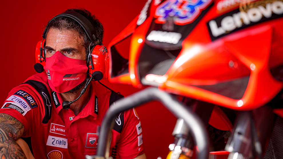 A mechanic in a red outfit is sitting next to a red motorcycle.