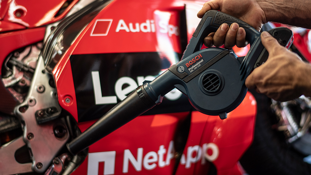 A person holds a Bosch Professional hairdryer in front of a red racing car.