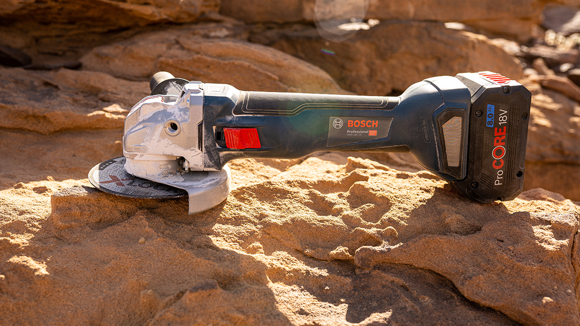 A Bosch Professional angle grinder is lying on sandy ground.