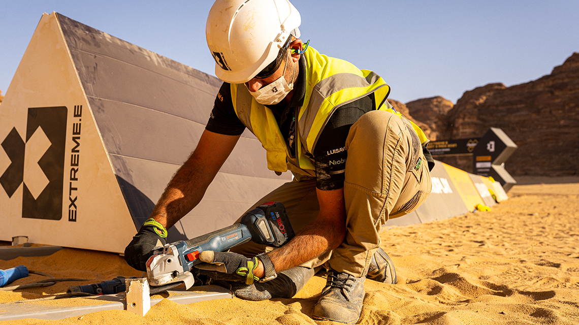 A worker uses a Bosch tool in a sandy environment.